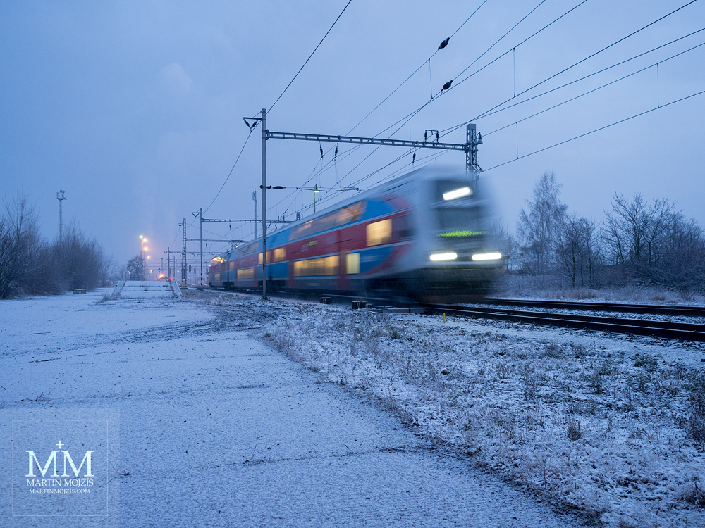 Osobní vlak odjíždí ze zasněžené stanice v mrazivém zimním ránu. Fotografie vytvořena objektivem Olympus 12 - 40 mm 2.8 Pro.